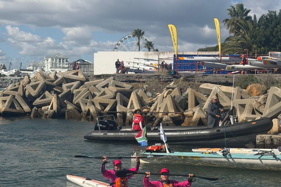 Bridget Boulle and Angela Taylor paddling into the finish of the 2026 Prescient Freedom Paddle with arms raised, the Ferris wheel and V&A Waterfront visible in the background