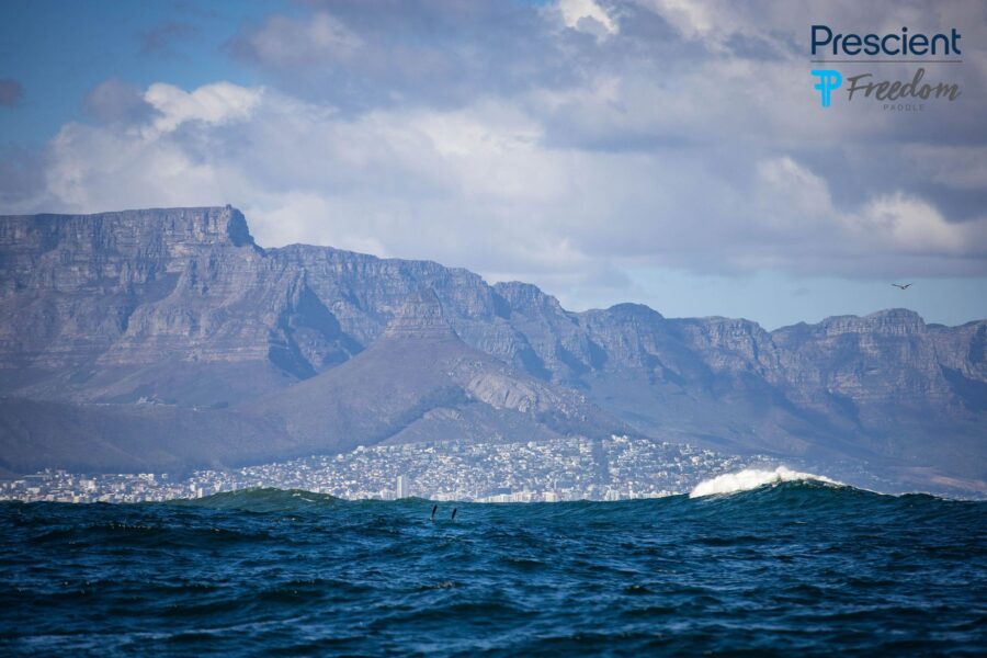 Paddlers dwarfed by massive swells with Table Mountain and Cape Town skyline in the background at the 2026 Prescient Freedom Paddle around Robben Island